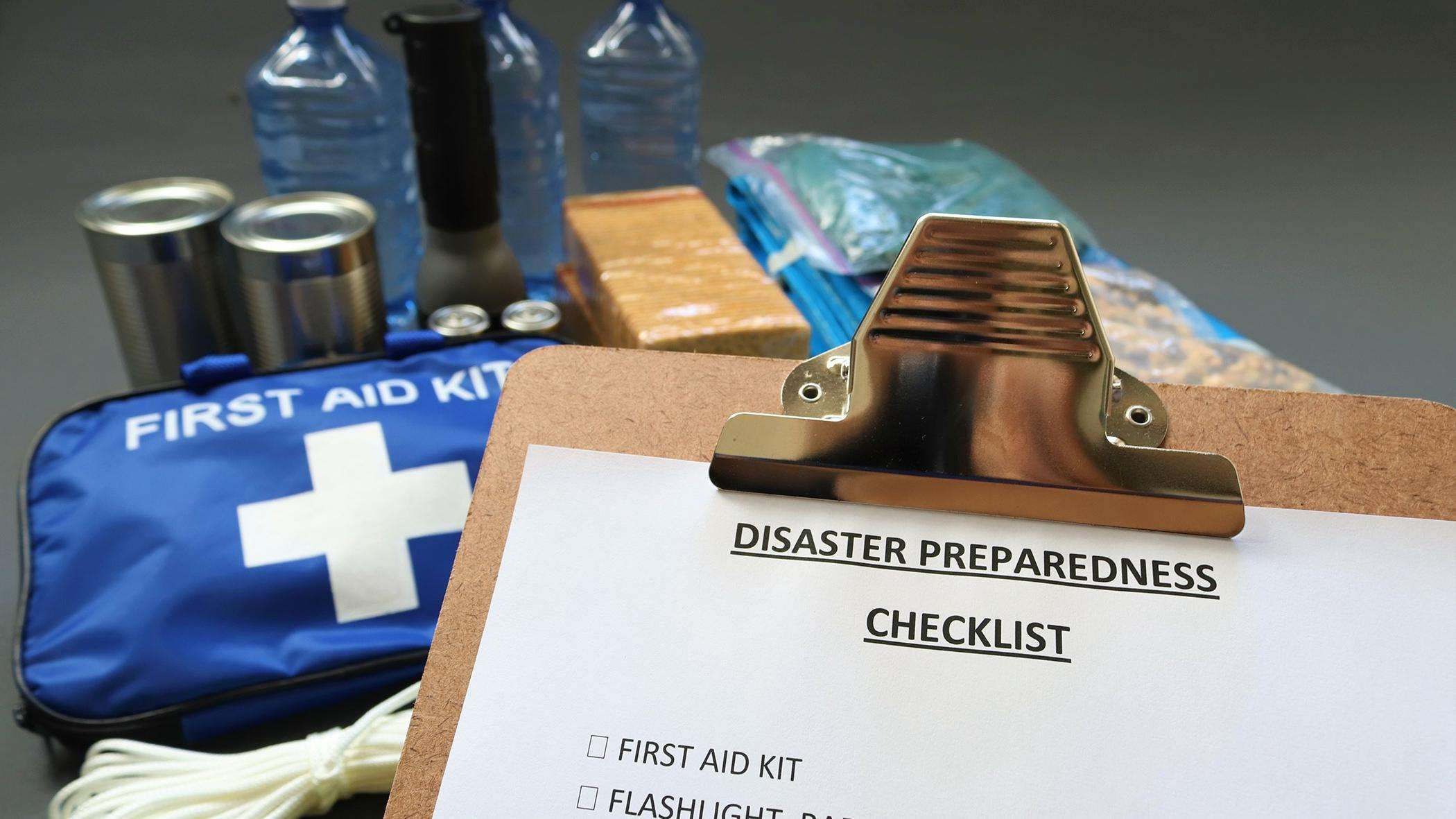 Disaster preparedness checklist on a clipboard with disaster relief items in the background