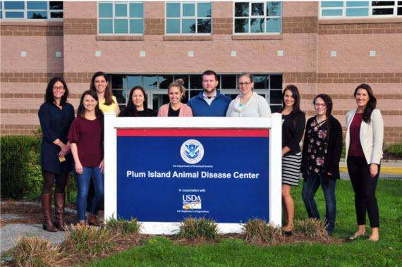 group of people standing behind the sign of the Plum Island Animal Disease Center