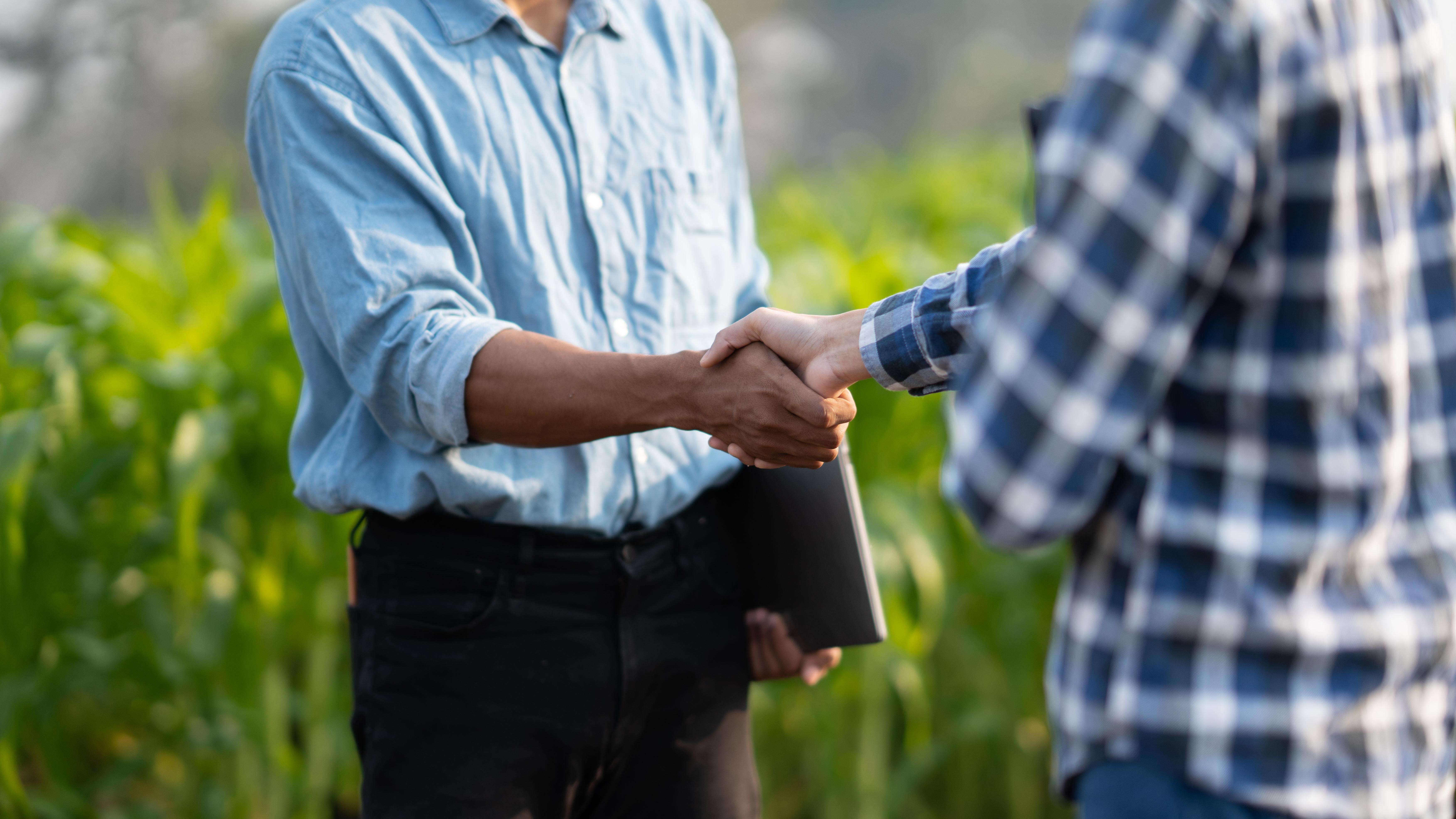 Close up of two farmers shaking hands with crops field background