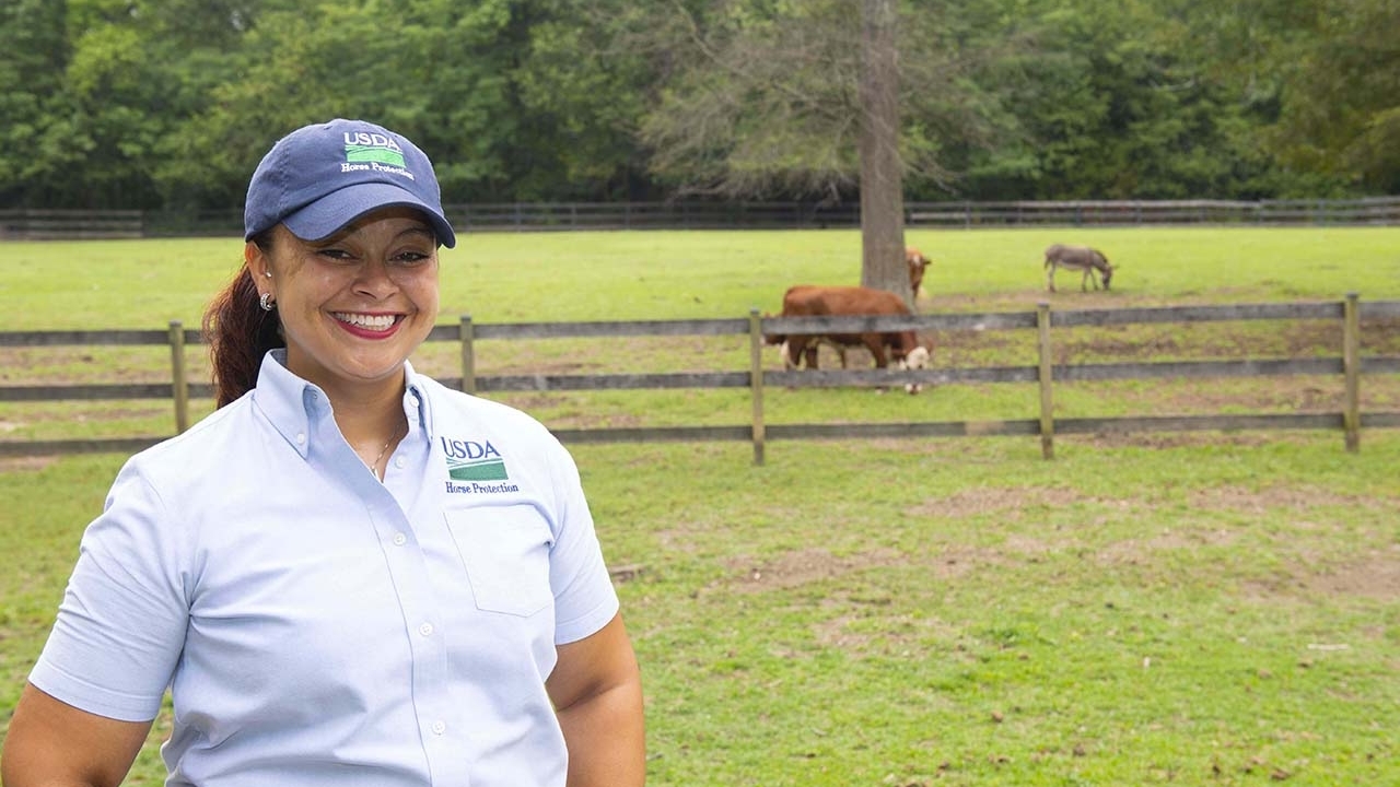 Woman wearing USDA ballcap standing in a horse field