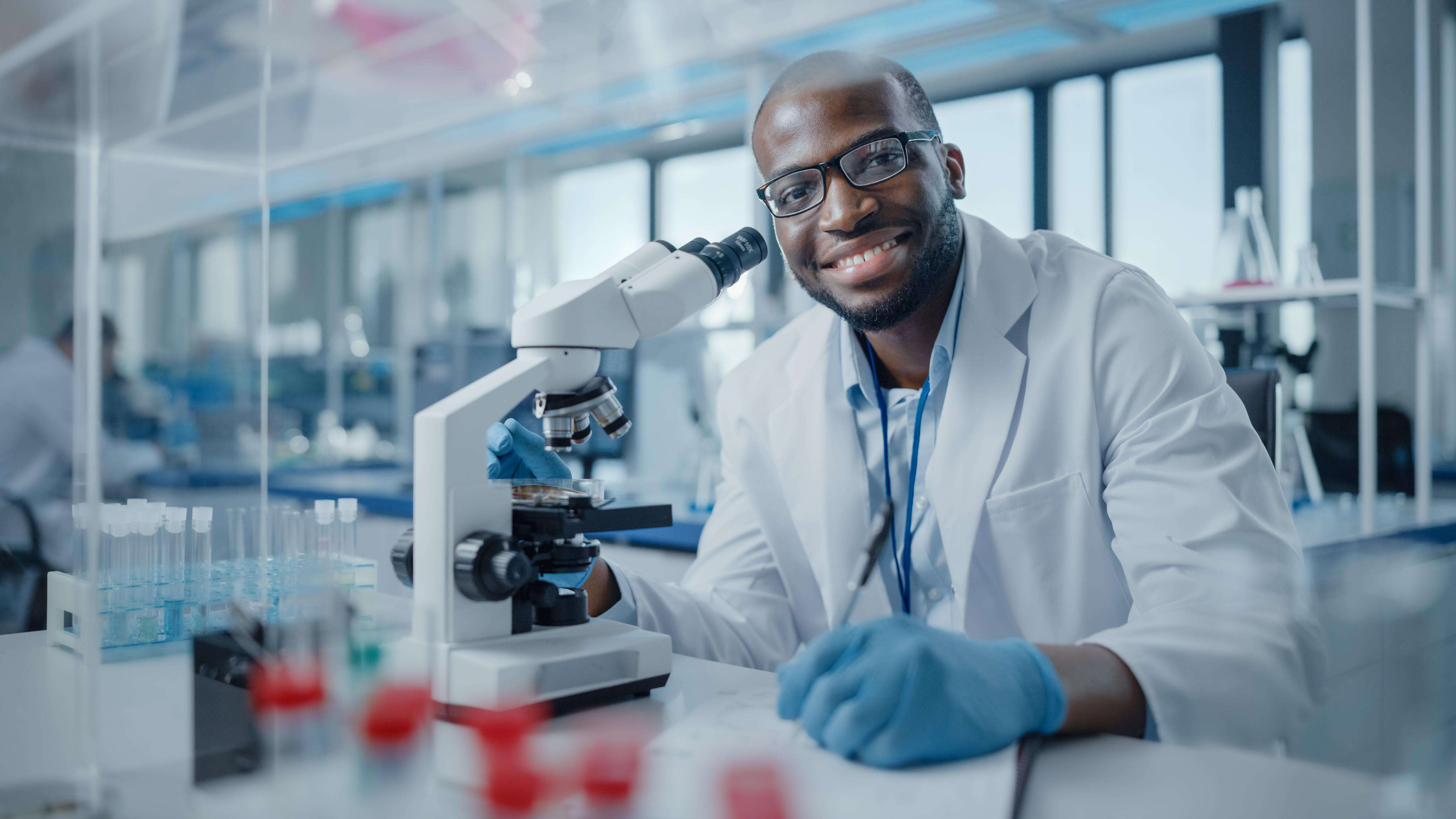photo of a smiling man in a white lab coat with a microscope 