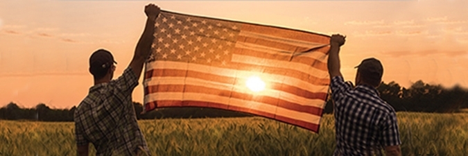 photo of two farmers in a field holding an American flag between them