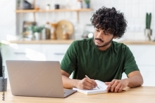 Man looking at computer while writing