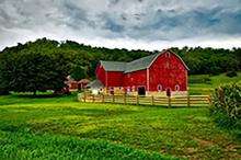 photo of a red barn in a field, surrounded by a wood fence, with trees behind it
